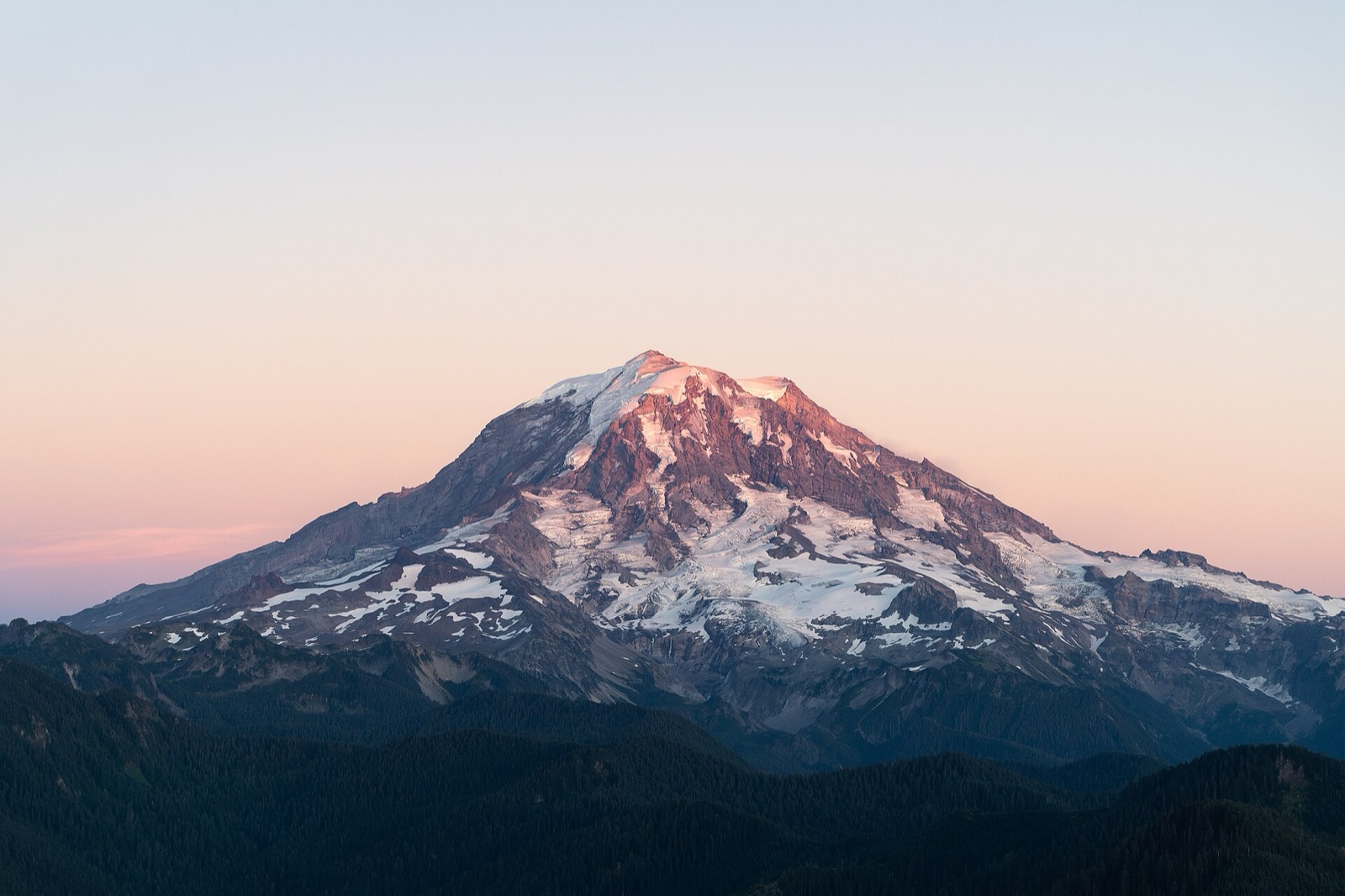 Mount Rainier at sunset, snowfields lit pink above dark ridges